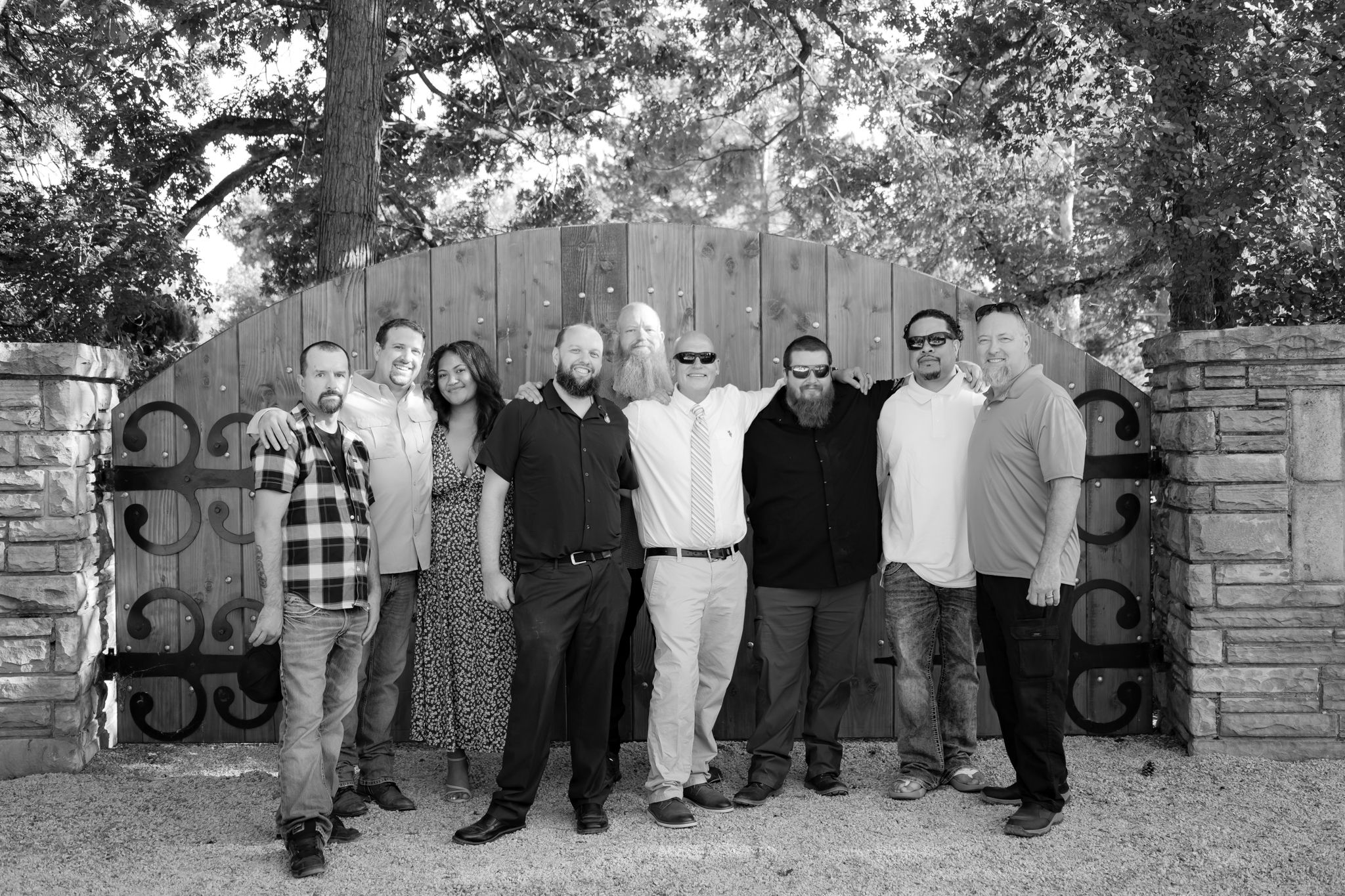 A group photo of wedding attendees posed in front of a decorative wooden gate.