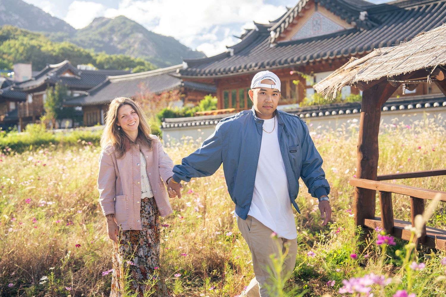 Couple enjoying a romantic stroll through a traditional Korean village with mountains in the background.