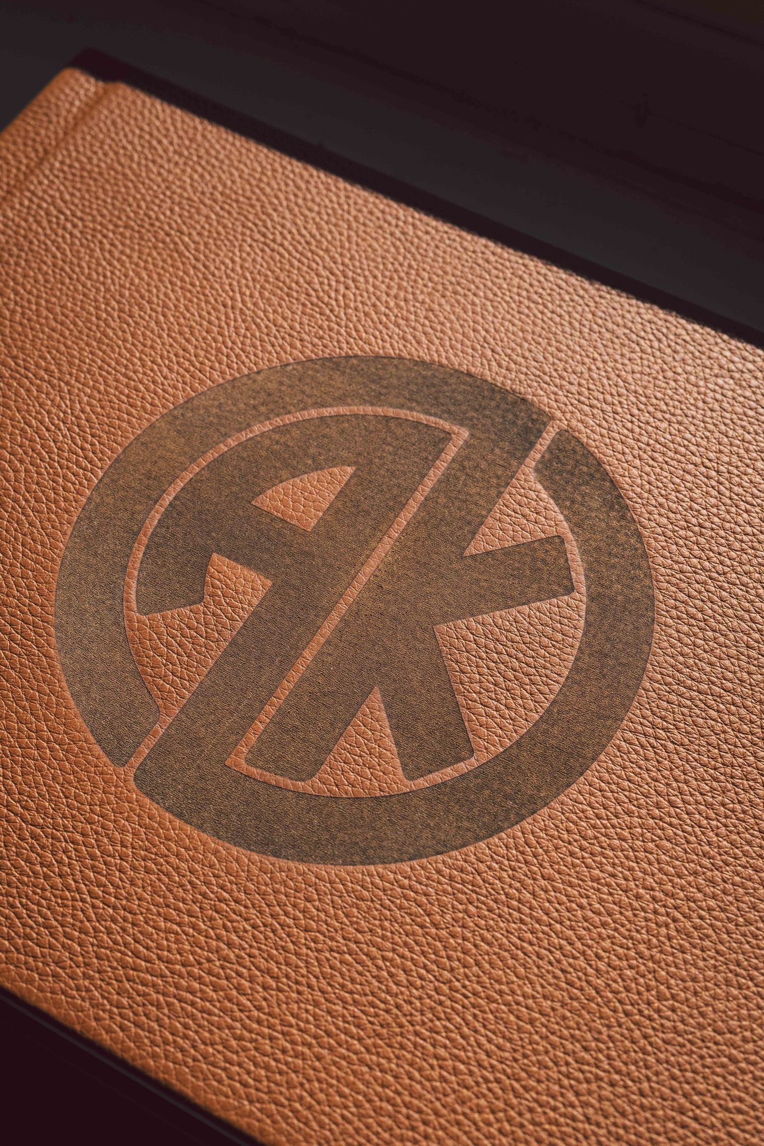 Close-up shot of a brown leather surface with repeating embossed logo pattern creating a textured design.