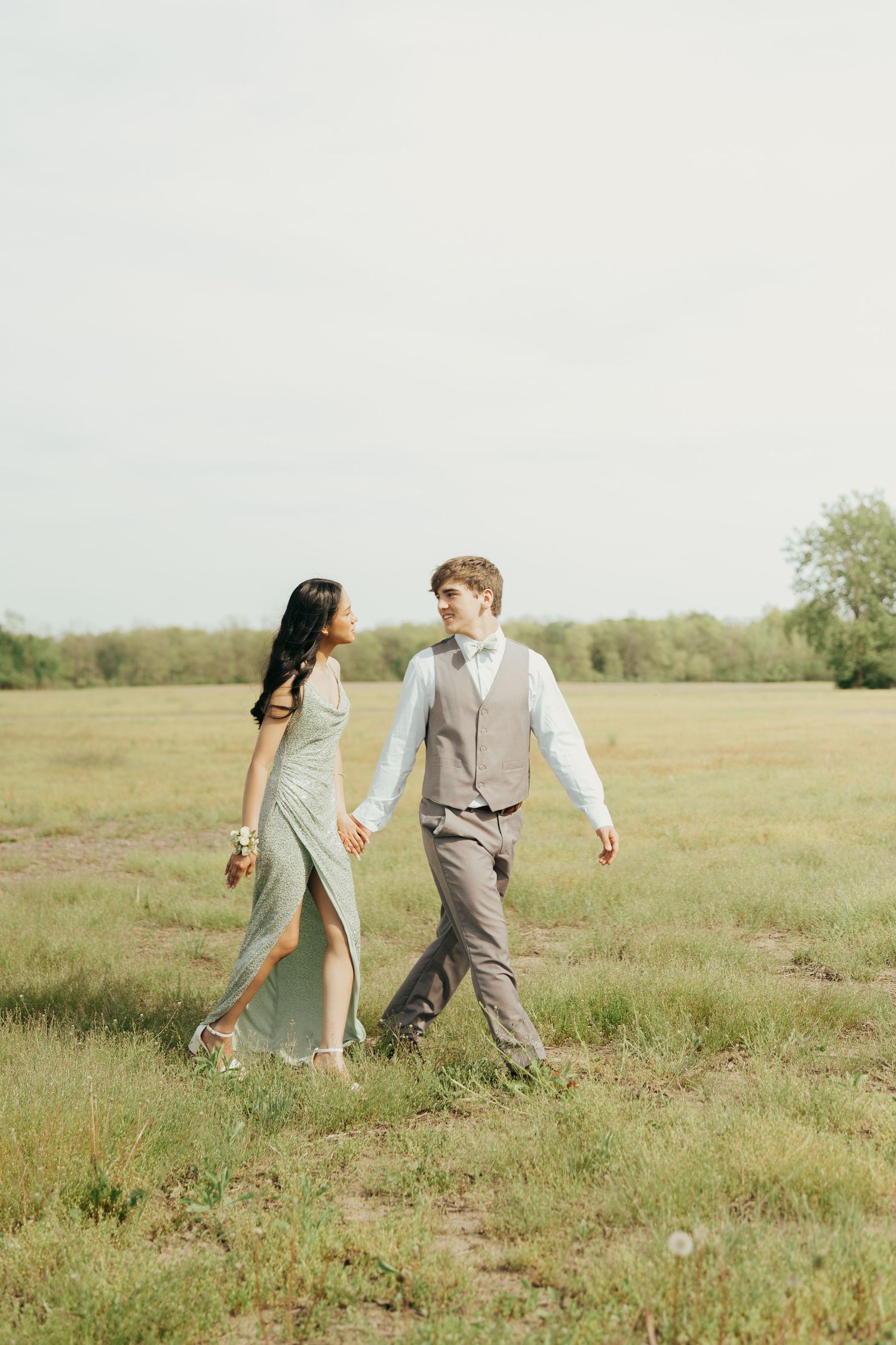 A couple walks hand in hand through a serene meadow on a bright summer day.
