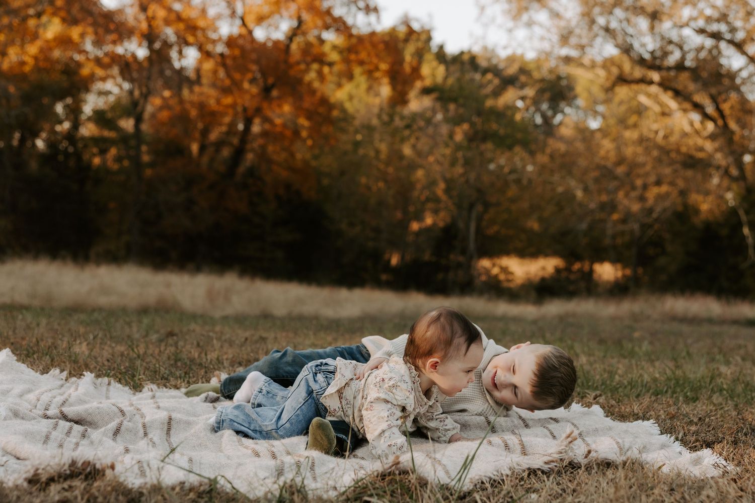 People lying on a blanket in an autumn field during golden hour.
