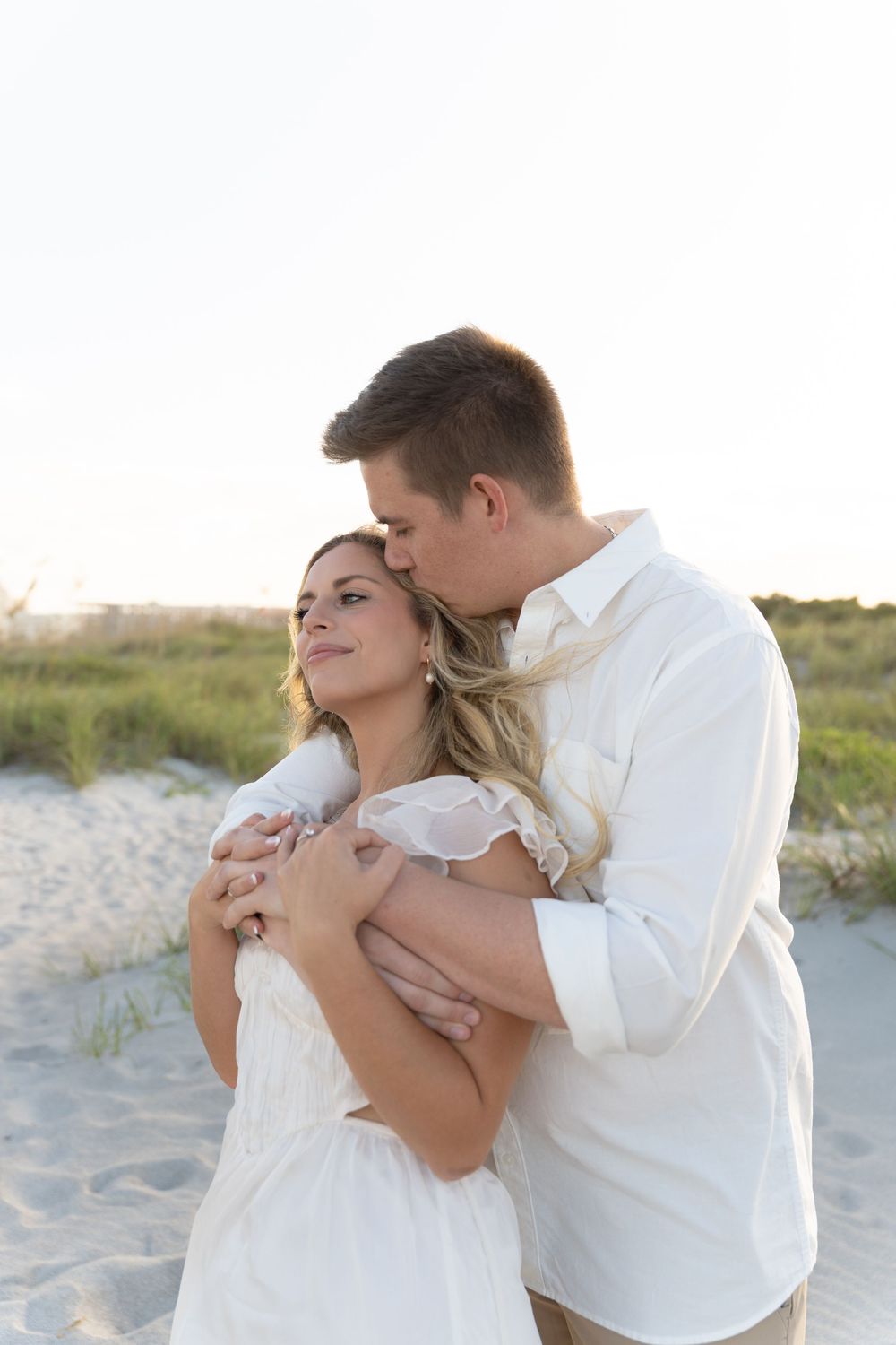 A romantic beach photoshoot with a couple in white attire embracing on sandy shores.
