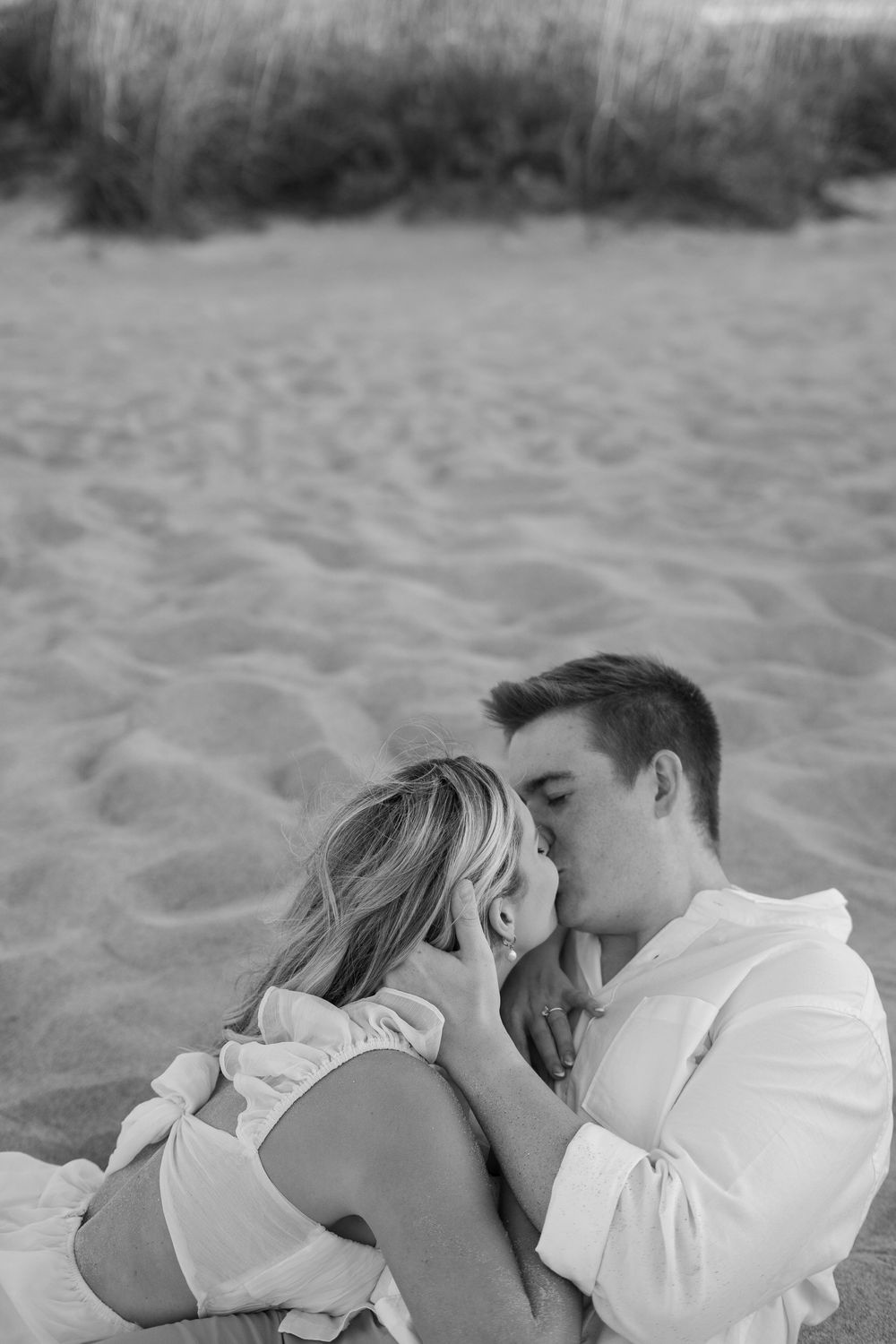 A romantic couple embracing while lying on the beach sand in black and white.