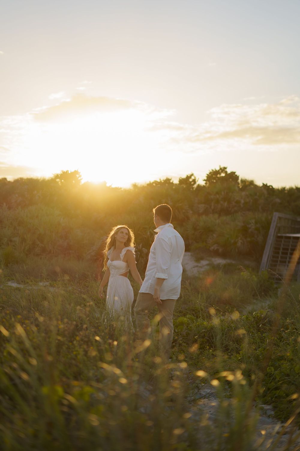 A couple strolls hand in hand along a coastal path at sunset with golden light illuminating the scene.