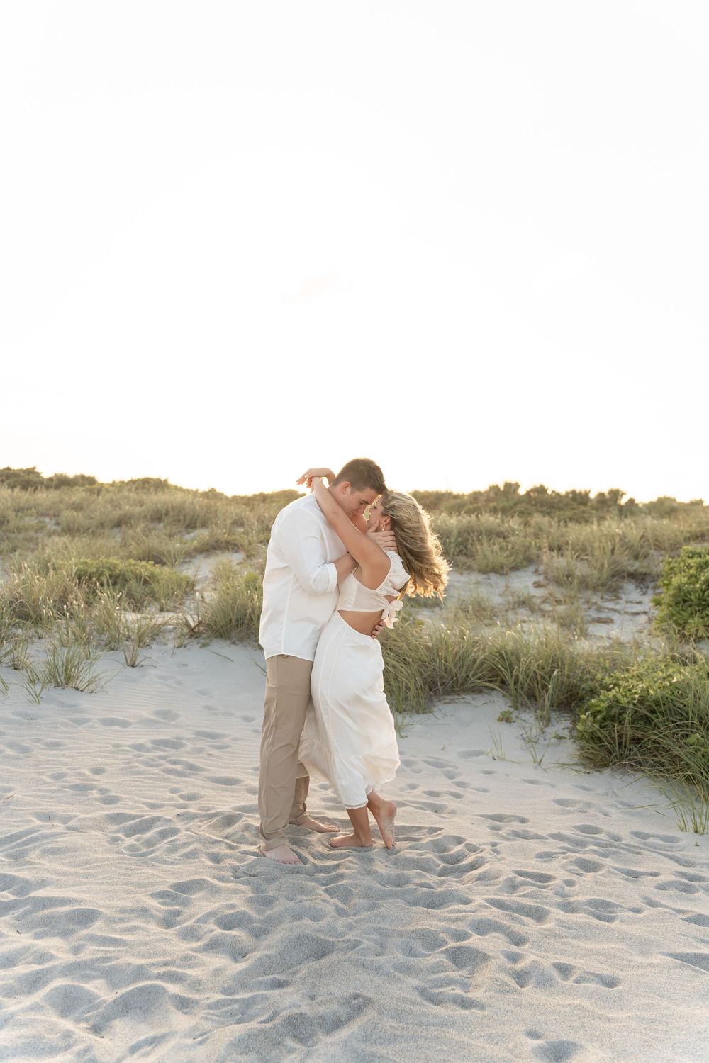 Couple dances and embraces on sandy beach dunes during a romantic sunset photoshoot.