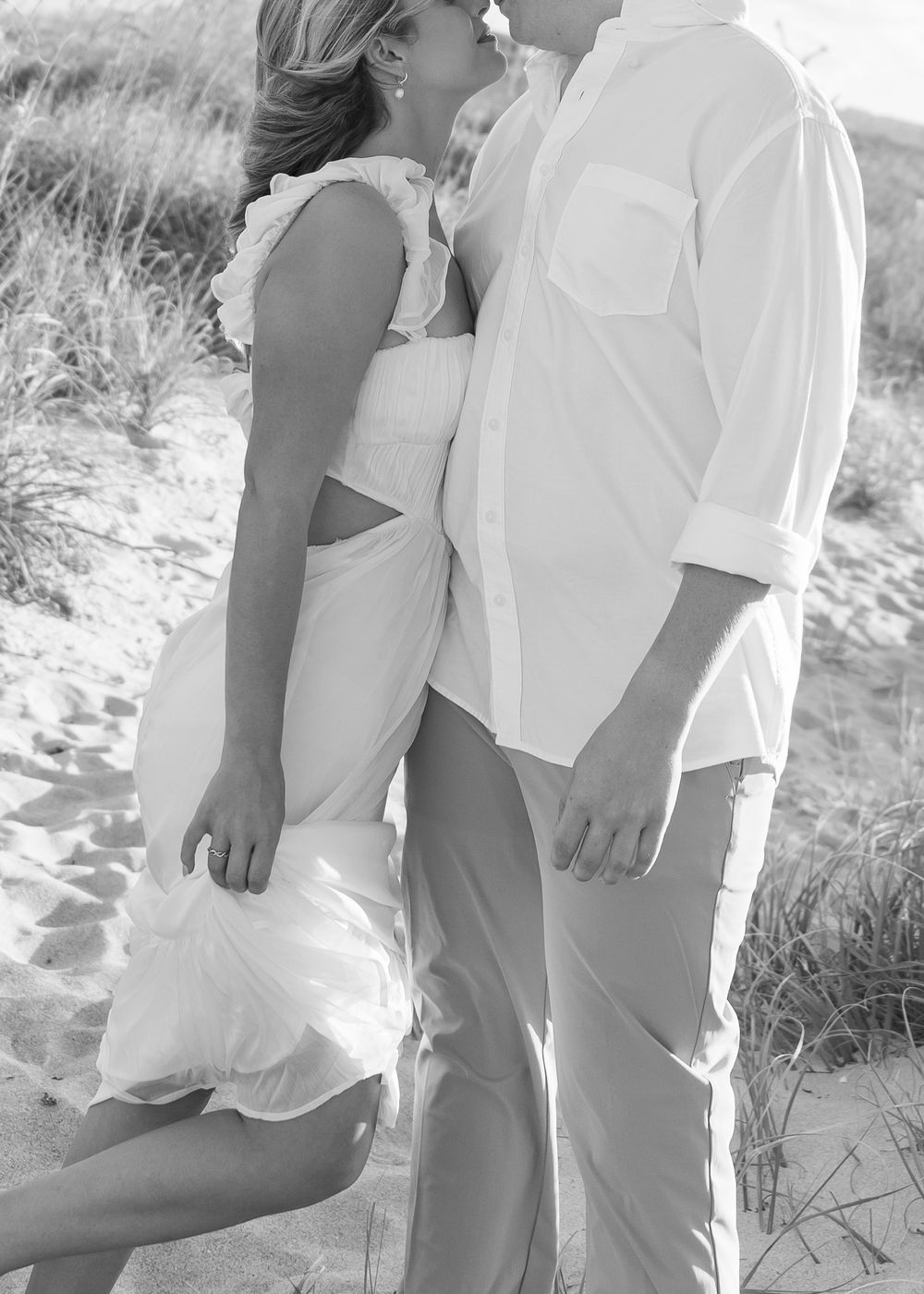 A couple in white outfits sharing an intimate moment on a sandy beach.