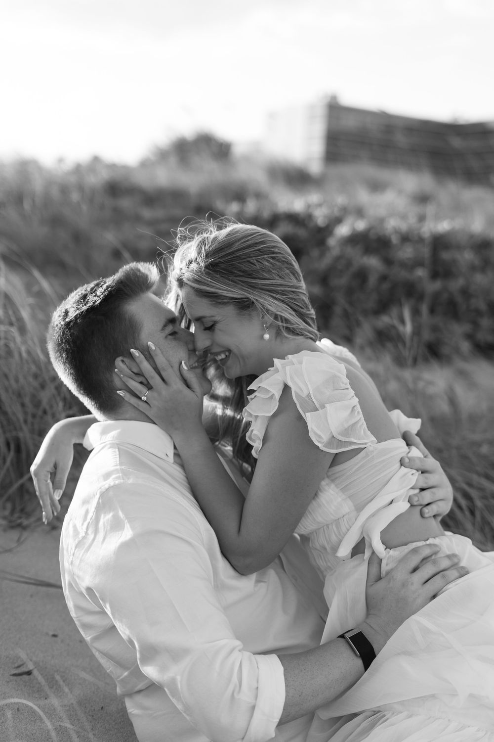 Black and white intimate portrait of couple sharing a joyful moment on beach dunes.