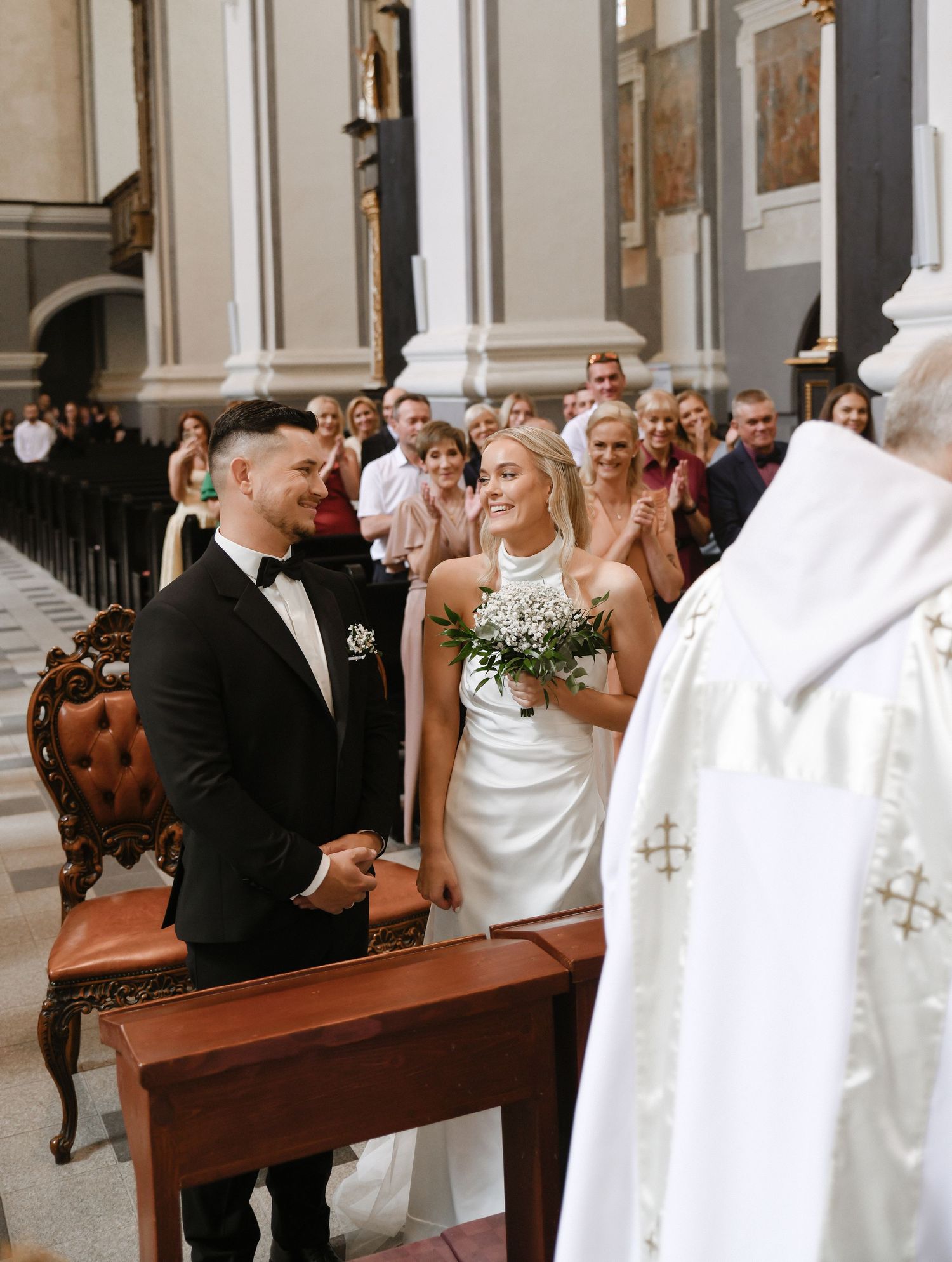 Wedding ceremony in a traditional church with wooden pews and elegant white decor during a Catholic mass service.