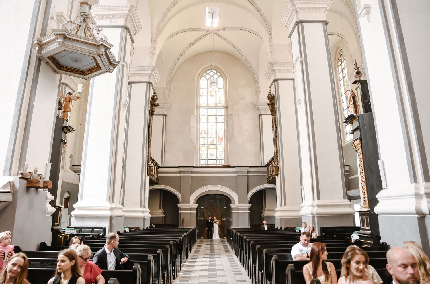 Interior view of a historic white church with vaulted ceilings, arched windows, and rows of wooden pews.