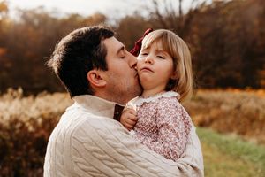 A couple embraces in a romantic outdoor autumn setting with golden light and natural surroundings.