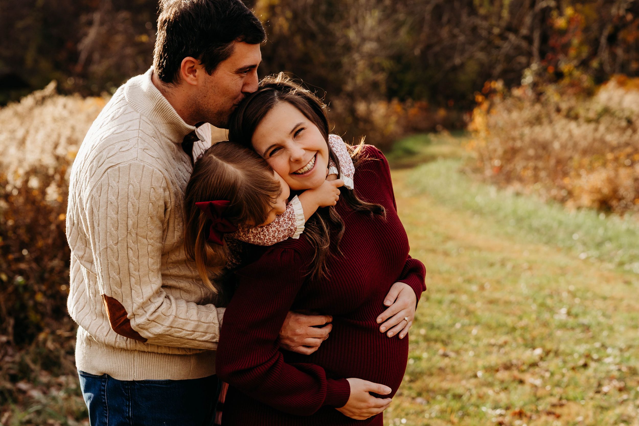 A romantic couple embraces in a sunny autumn field wearing cozy sweaters during their outdoor photo session.