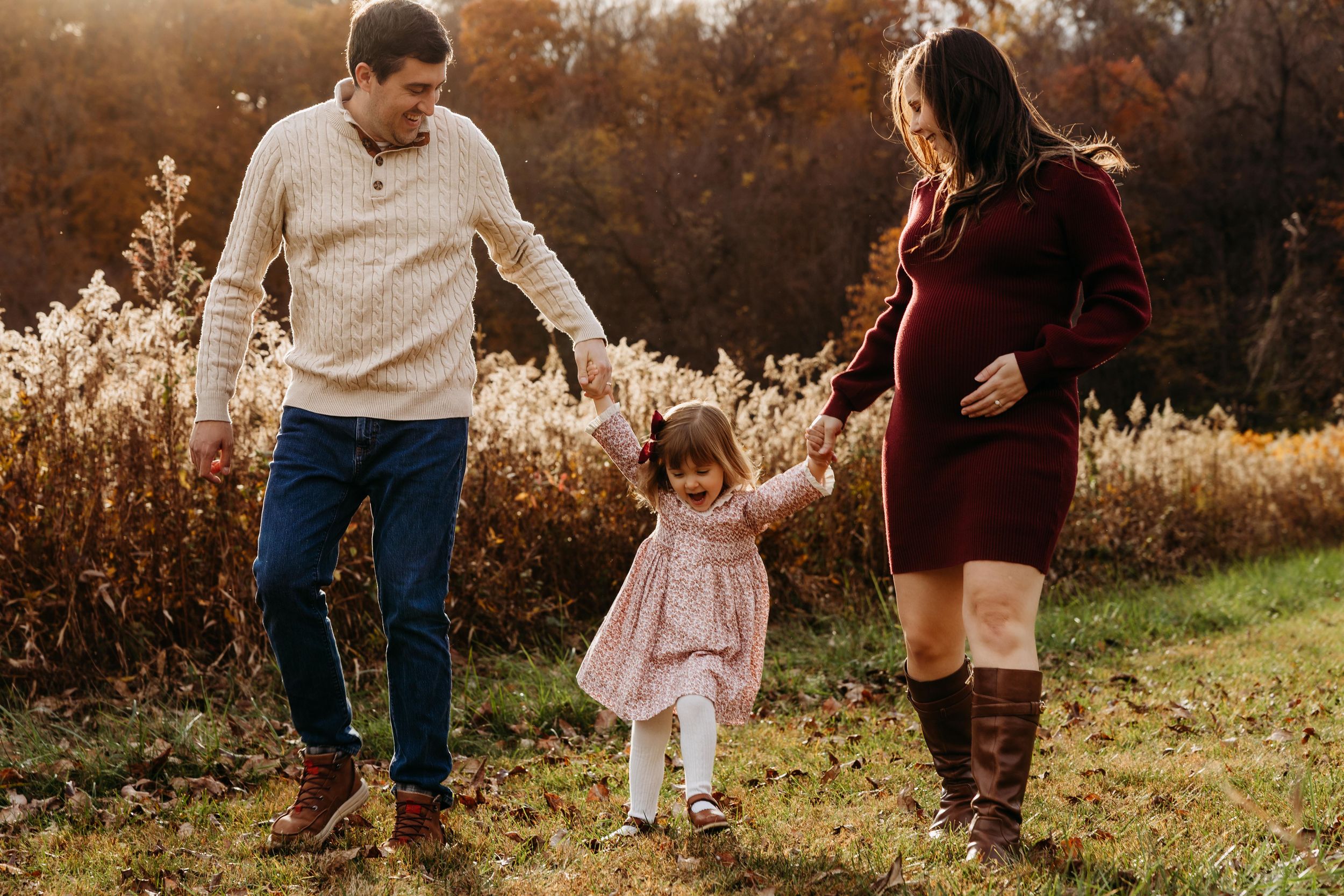 A family walking together in a golden autumn field during sunset with tall grass and trees in the background.