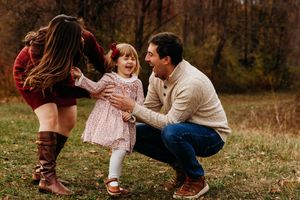 Family playing and having fun together outdoors in an autumn field during a fall photo session.