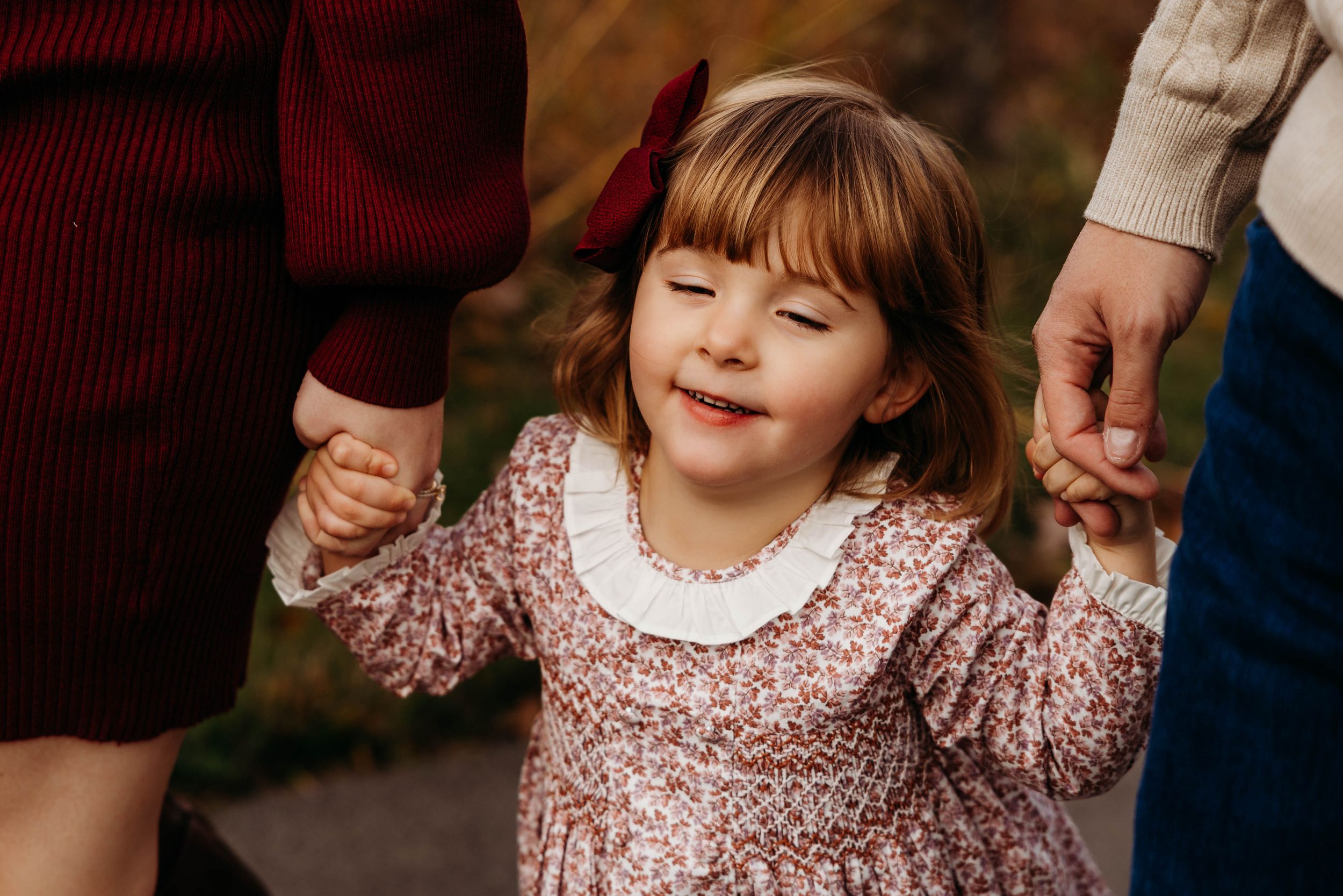 A child in a floral dress smiles and plays outdoors during a warm autumn day.