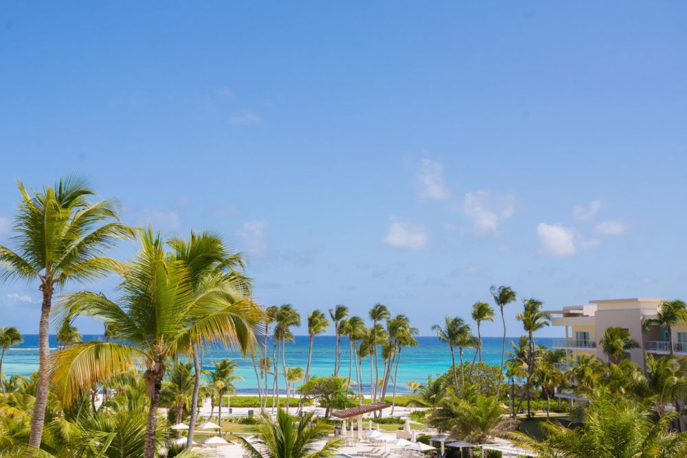 Palm trees sway along a pristine white sand beach with turquoise waters and luxury resorts in the Caribbean.