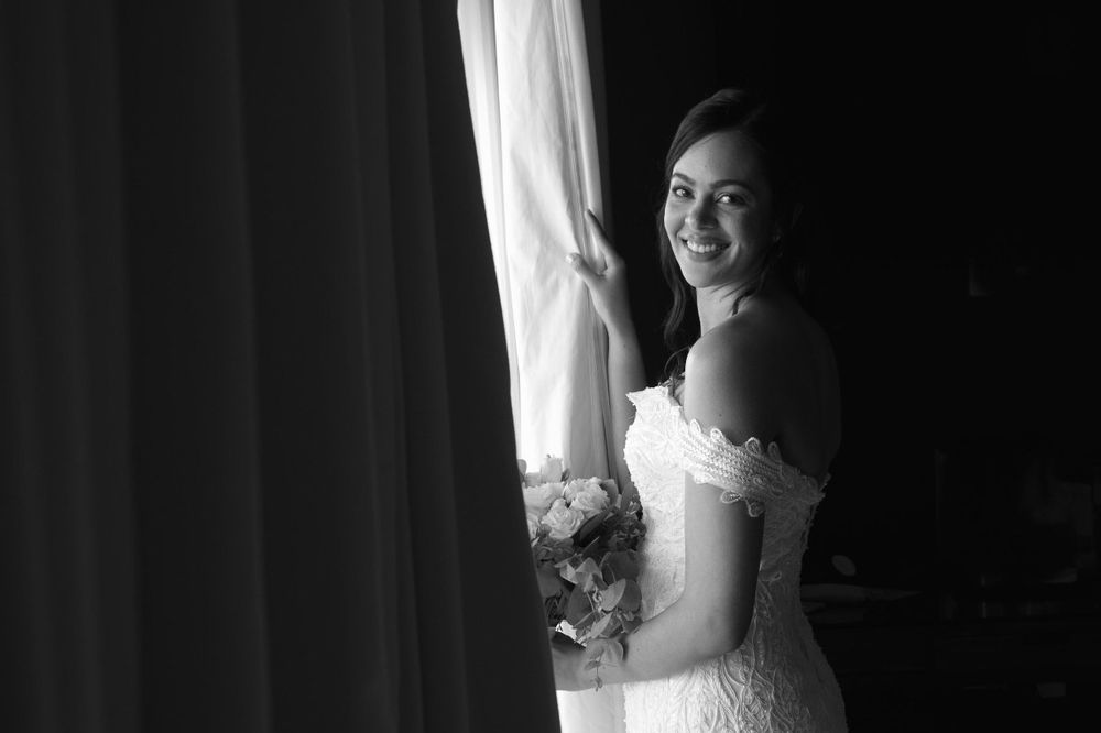 Black and white photos show a bride in her wedding gown posing by a window with natural light.