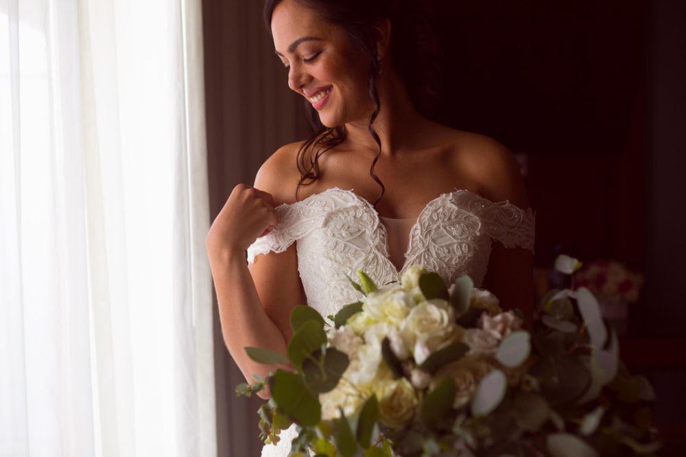 Elegant bride in white strapless wedding gown holds a stunning bouquet of white orchids and roses against a dark background.