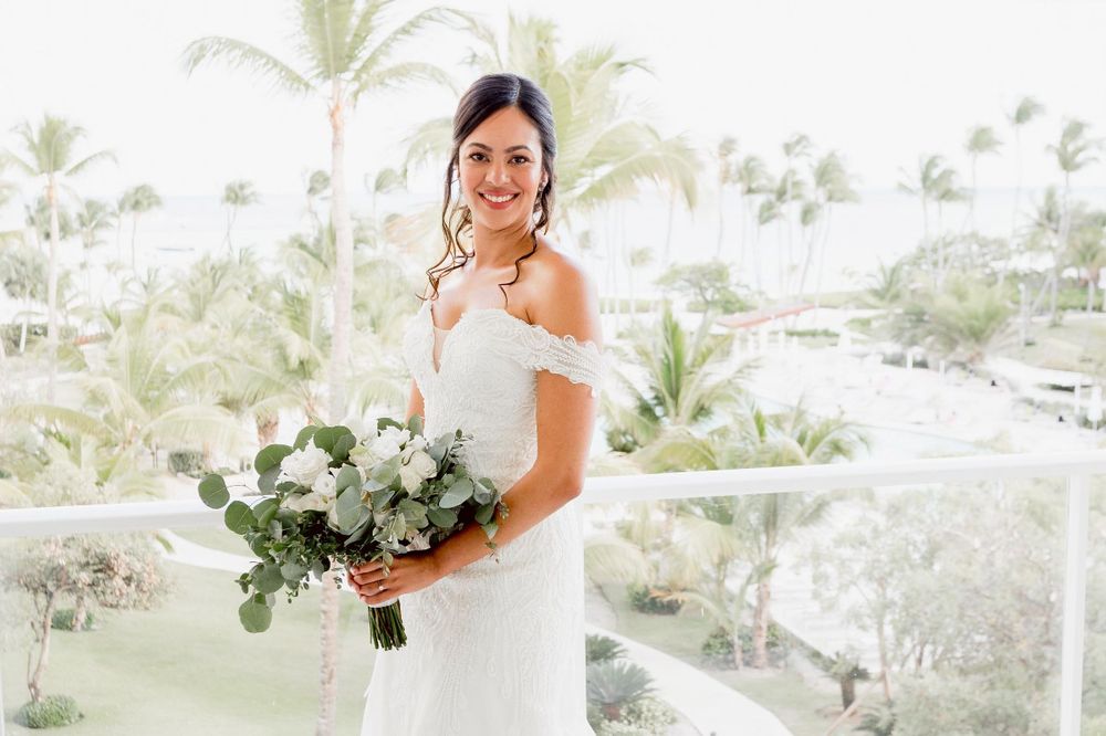 A bride holds a white and green floral bouquet while standing in an elegant outdoor venue with palm trees.
