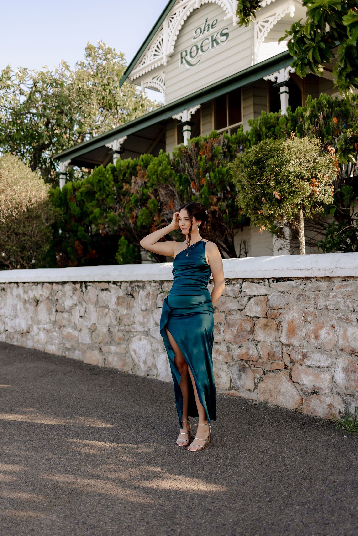 A sequence of fashion poses against a stone wall with a white building in the background.