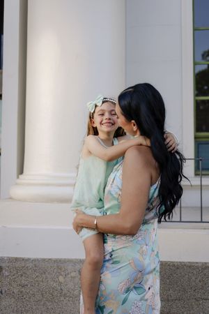 Mother and daughter share joyful moments together while posing near white pillars.
