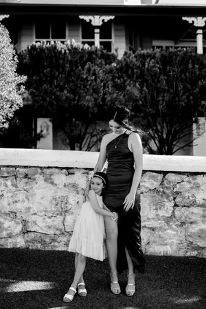 A black and white portrait of two figures in formal wear standing by a stone wall.