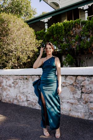 A figure in a teal satin dress poses against a stone wall and garden backdrop in a series of outdoor portraits.