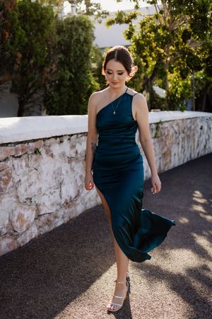 Woman in navy blue dress twirls and dances in sunlit outdoor setting.