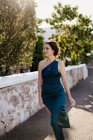 Woman in navy blue formal dress poses along stone wall path during golden hour sunset.