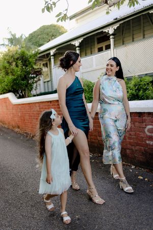 People in coordinating dresses pose playfully along a brick wall outside a historic building.