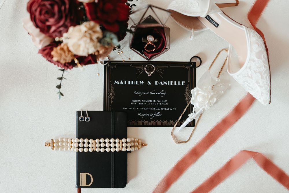 Wedding accessories including pearls, invitations, and floral details arranged on a pink and white surface.