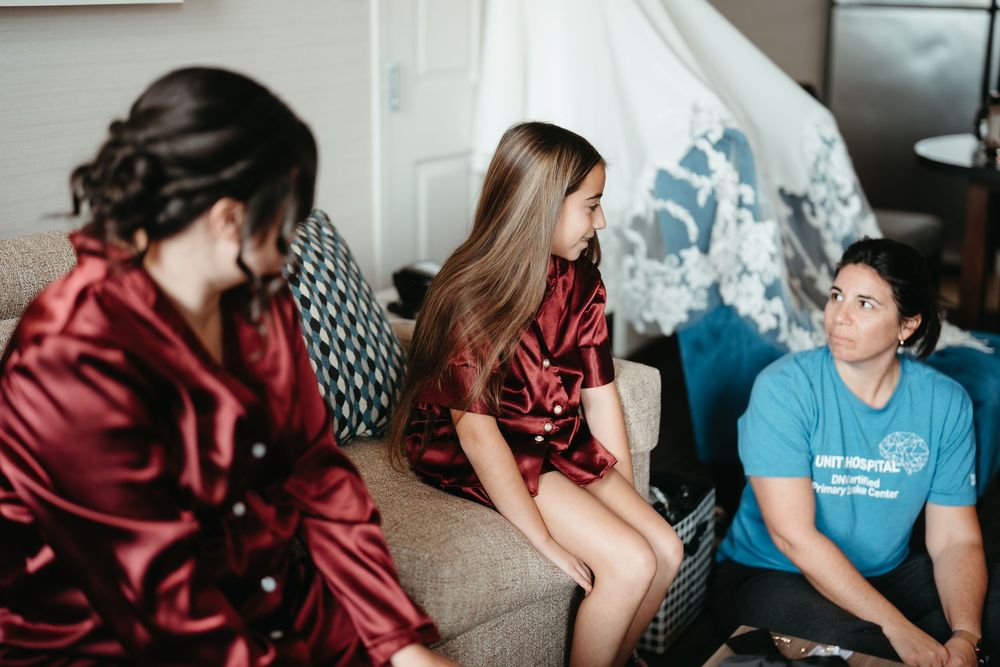 Three people having a conversation in a living room, with two wearing burgundy satin robes and one in a blue t-shirt.