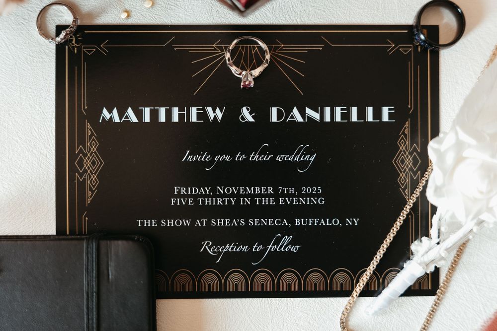Luxurious black wedding invitation with gold art deco patterns and modern typography laid on white surface.