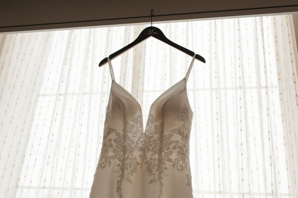 A row of elegant white wedding dresses hanging on display against sheer curtains in a bridal boutique.