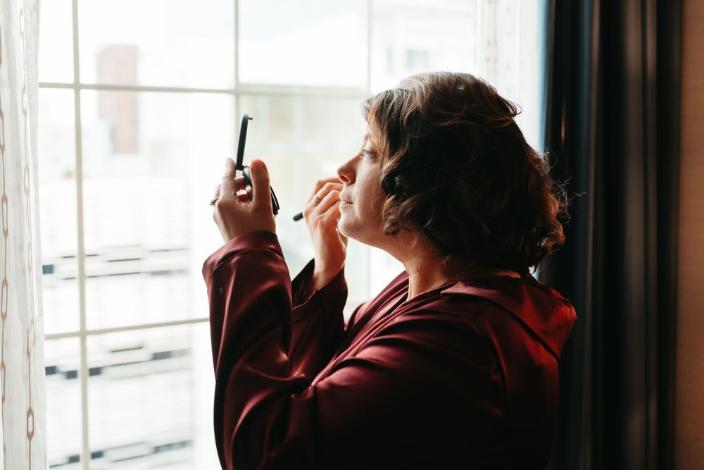 Person in a burgundy hoodie stands against a bright window, creating a silhouetted profile view.