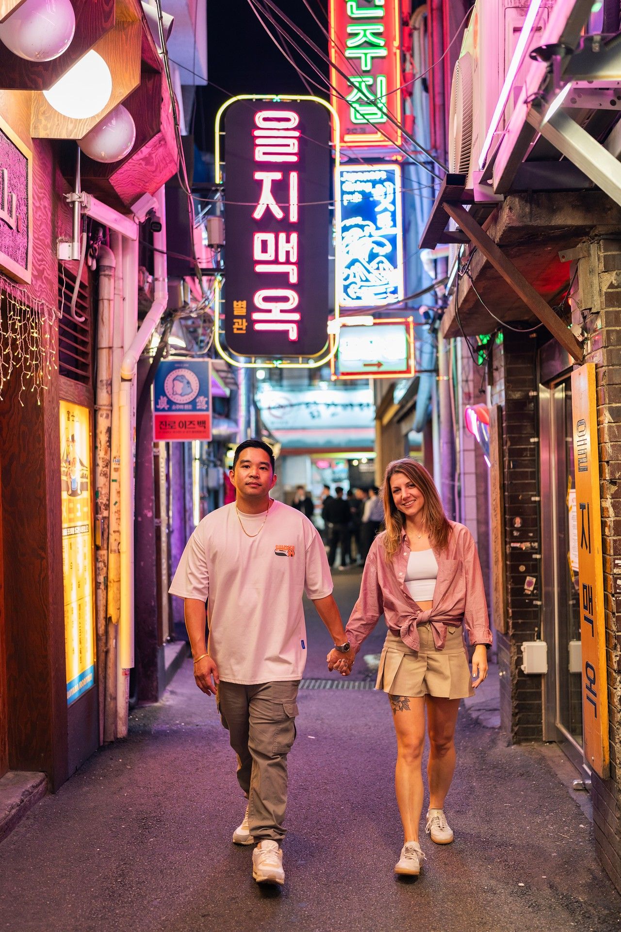People walking through a vibrant neon-lit alley in Seoul's nightlife district with colorful Korean signage.
