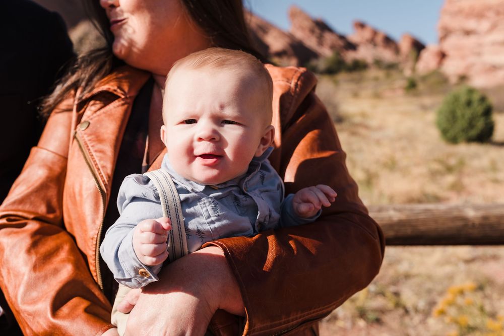 A small child in an orange jacket smiles while being held against a backdrop of red desert rock formations.