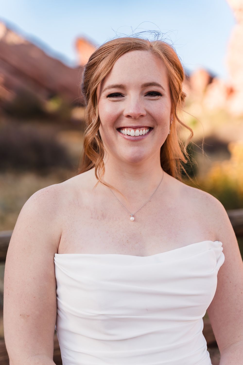 A bride in a white strapless wedding dress smiles warmly in an outdoor portrait session at sunset.