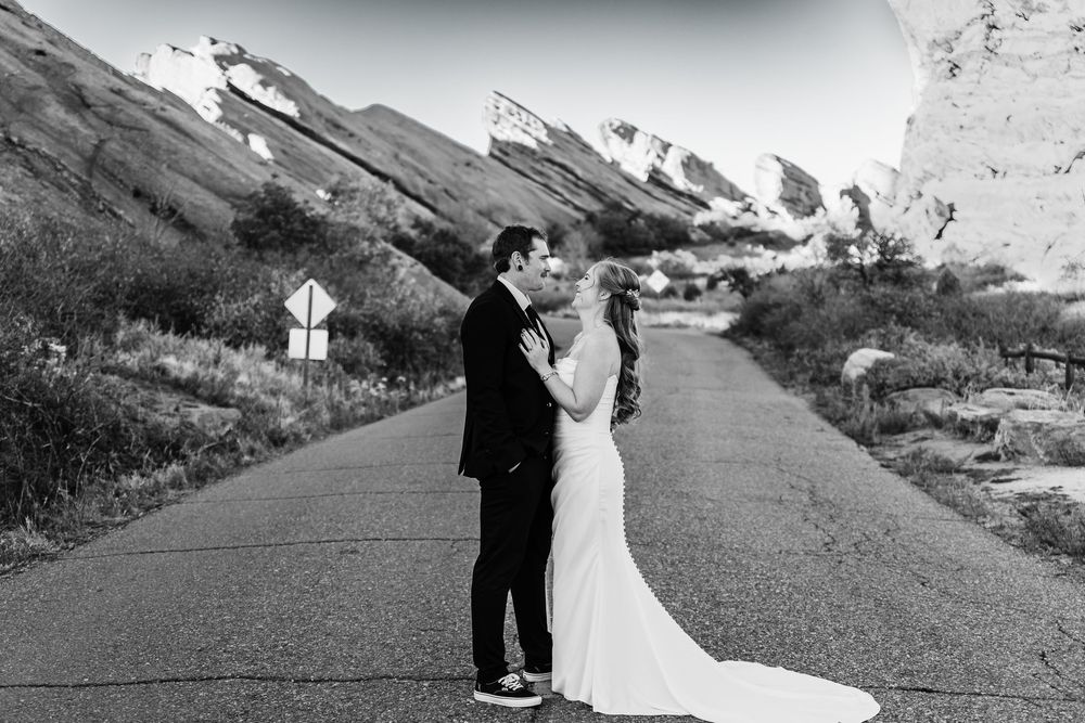 A couple shares an intimate moment on a scenic mountain road surrounded by snow-capped peaks in the distance.