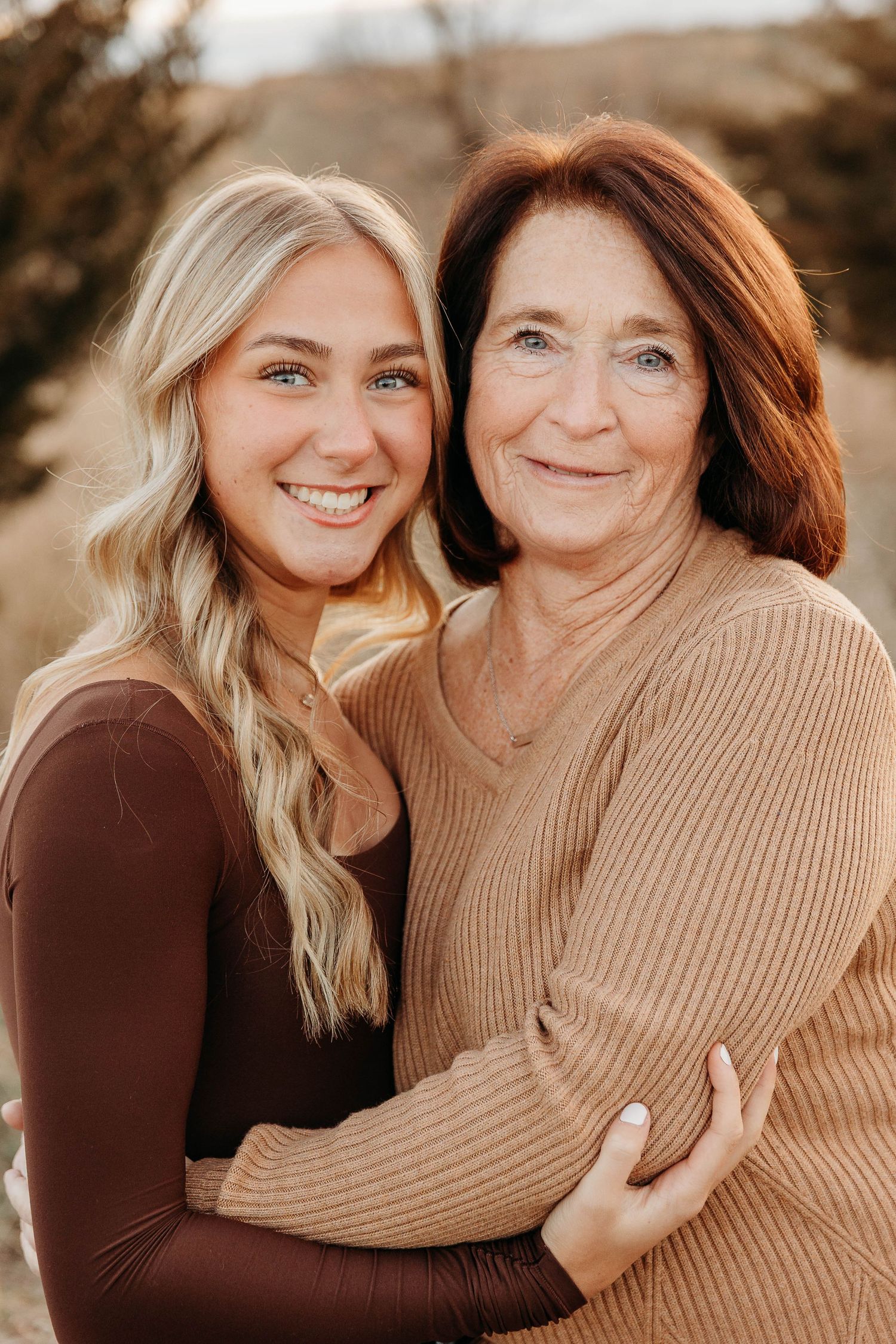 Close-up outdoor portrait of two people embracing and smiling while wearing brown and beige sweaters.