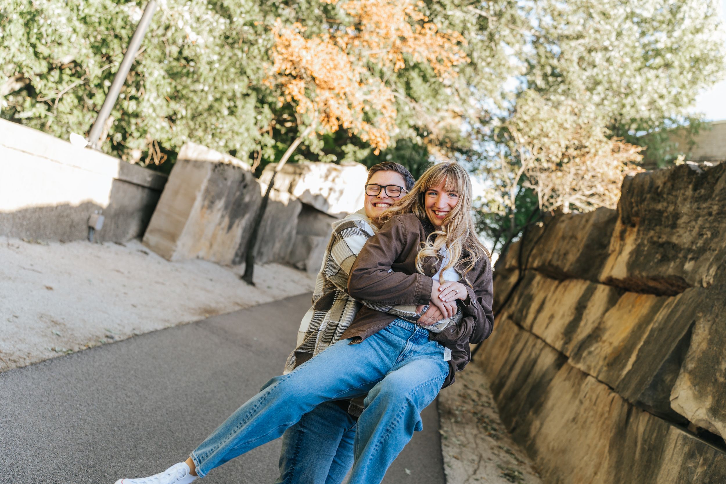 A couple embraces in a romantic pose against a stone wall during an autumn engagement photo session.