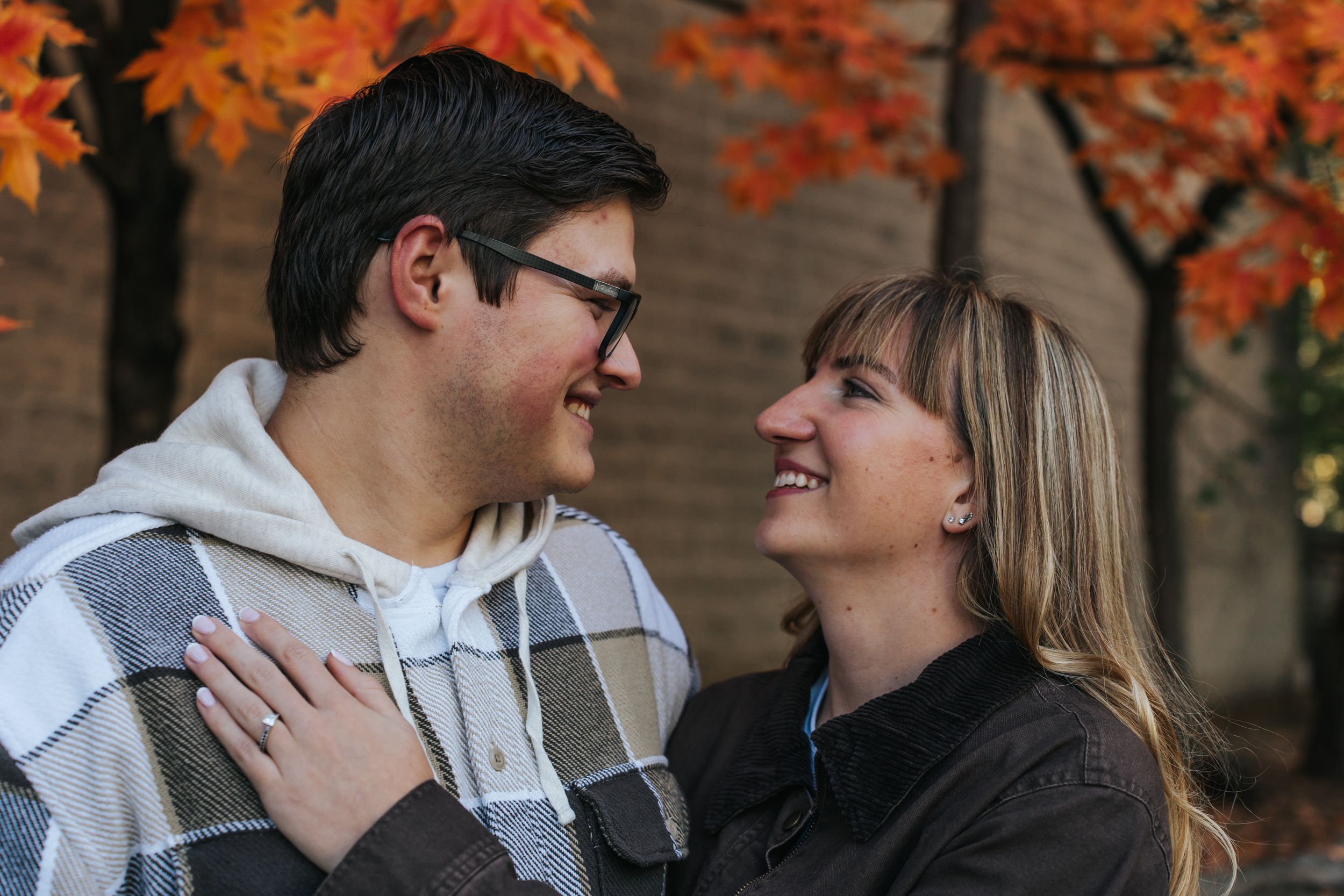 A couple shares a joyful moment together under vibrant orange autumn foliage.