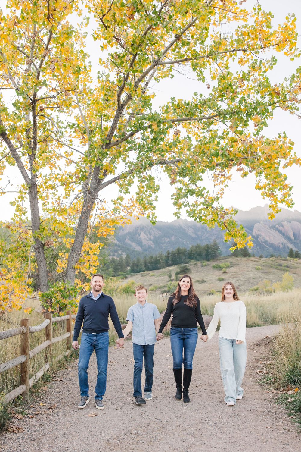 Family walking together on a mountain trail during autumn with golden leaves on trees in the background.