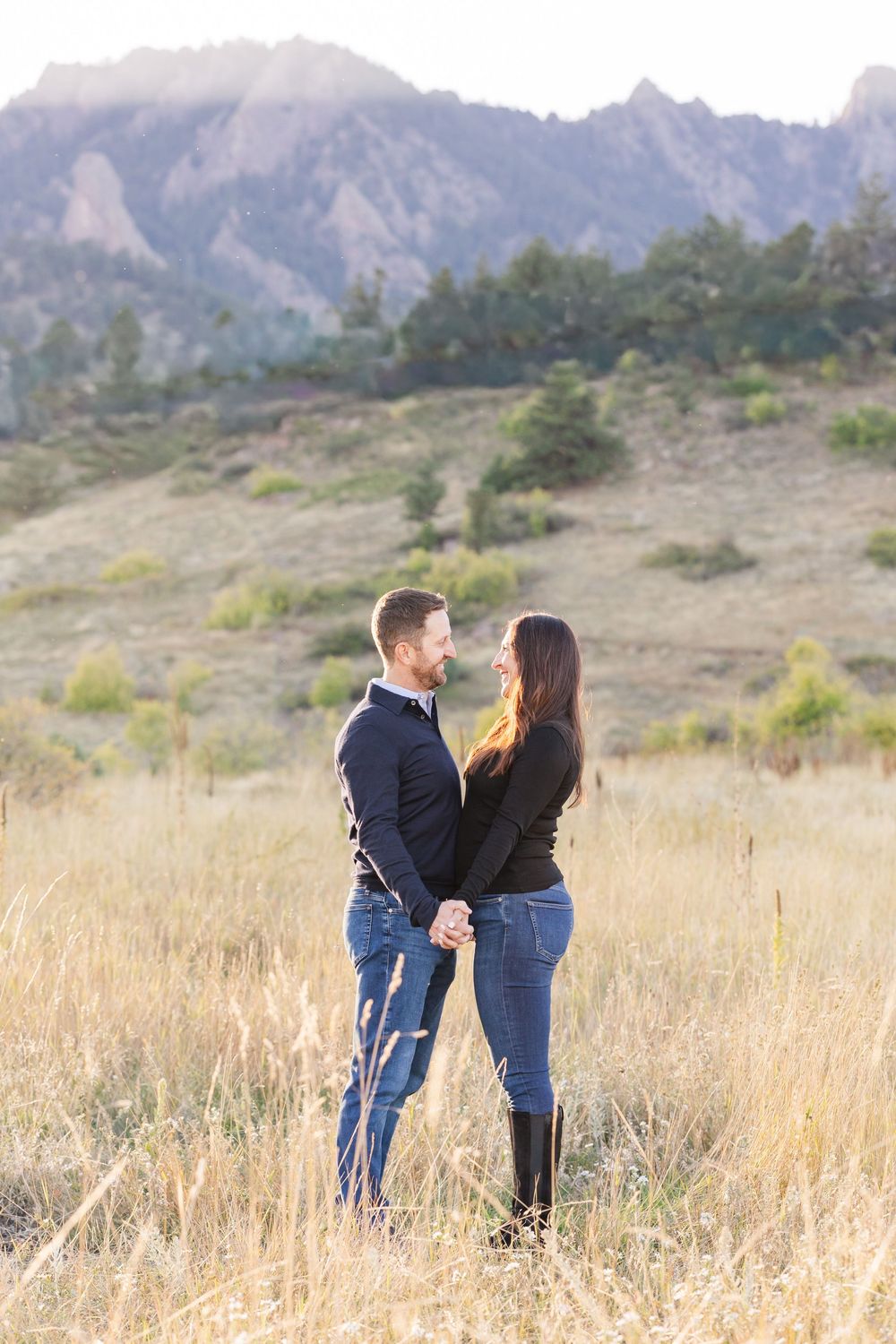 A couple shares a romantic moment in a field of tall grass with mountain peaks in the background.