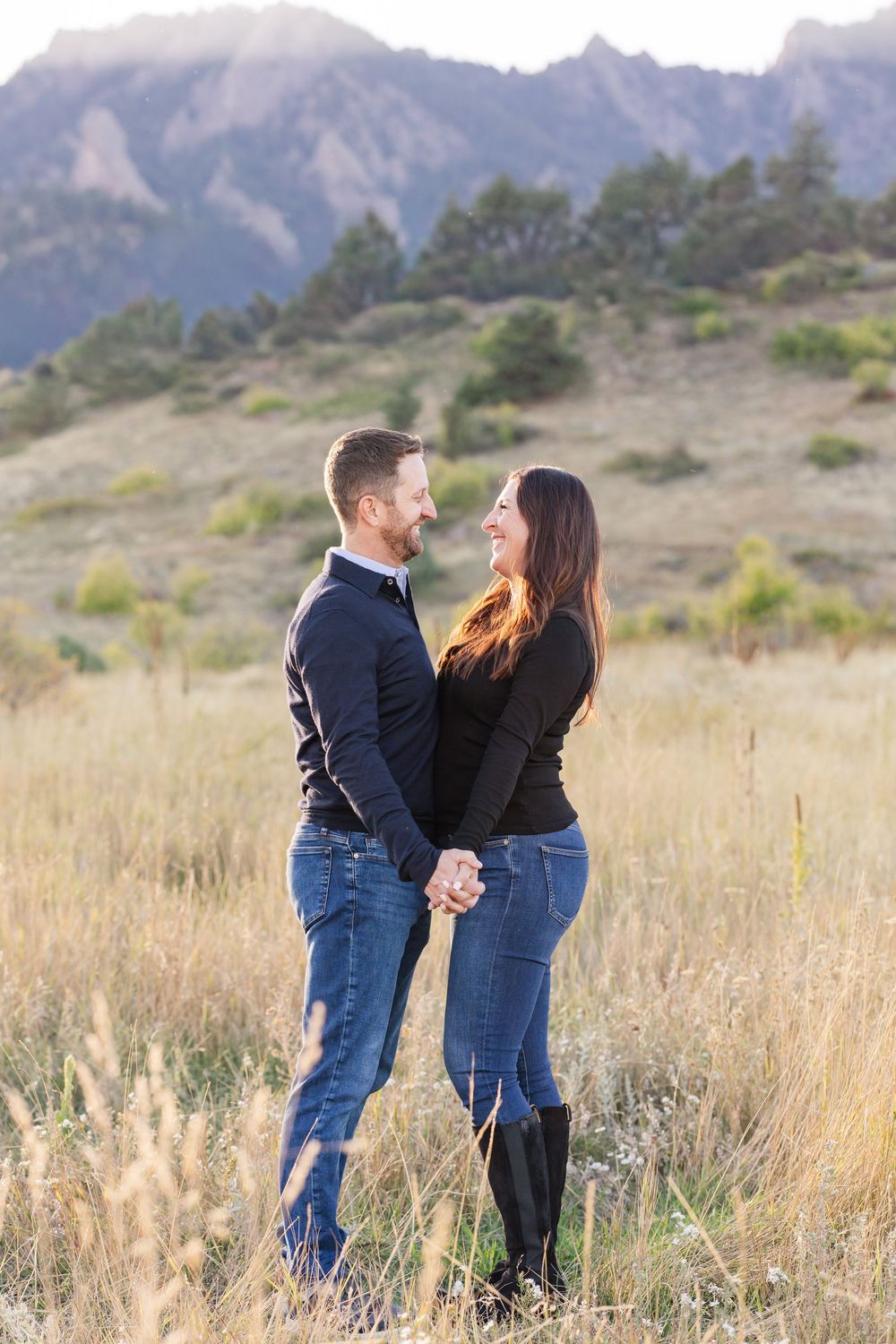 Couple standing together in a field of tall grass with mountain views.