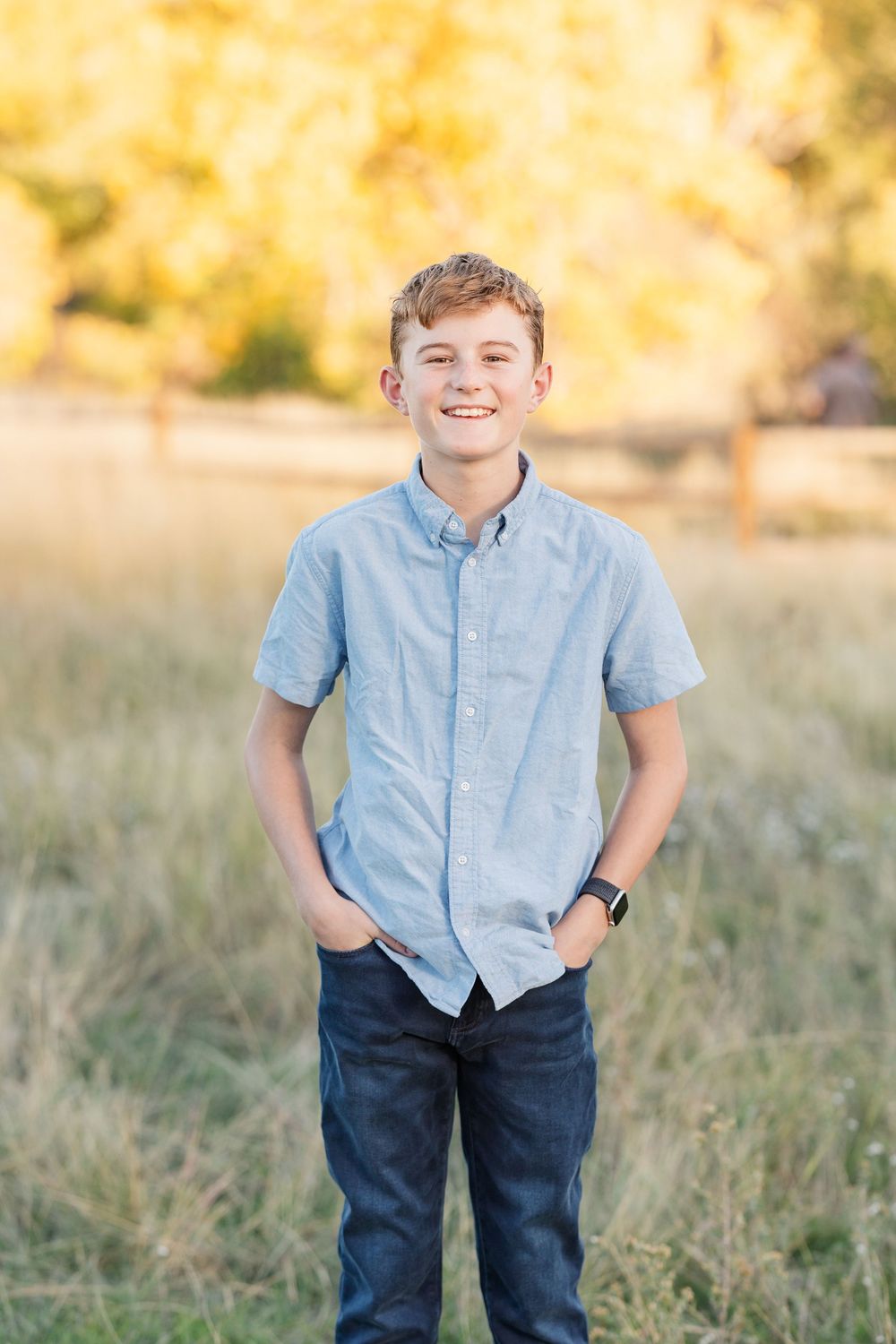 A young person in a light blue shirt and dark pants poses in a sunlit meadow.