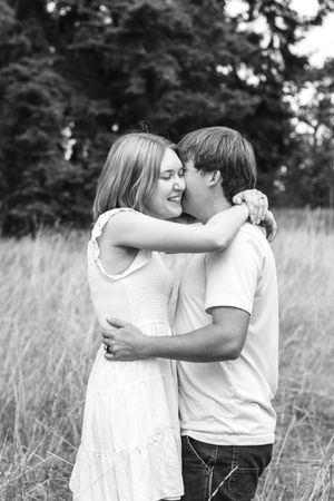 Black and white photo of a young couple embracing and smiling in a field.