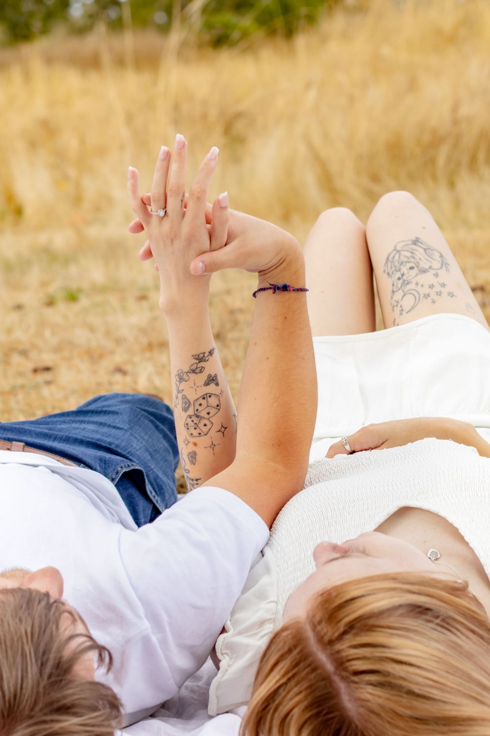 Newly engaged couple laying down and the man admiring the woman’s ring