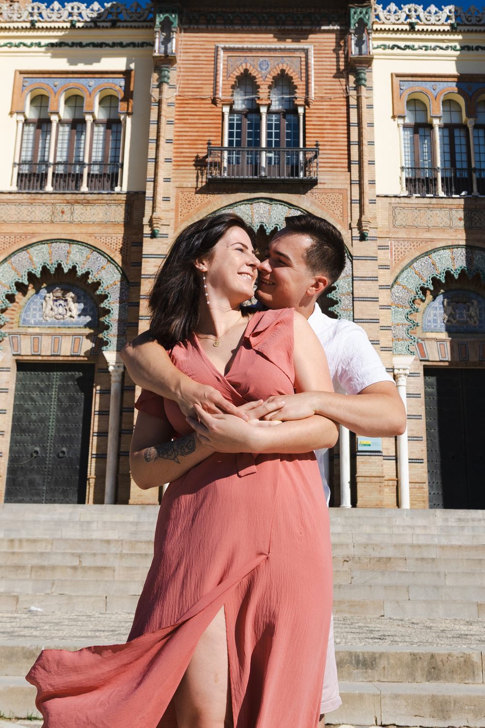 A couple shares romantic moments in front of ornate Spanish architecture at Plaza de Espana in Seville.