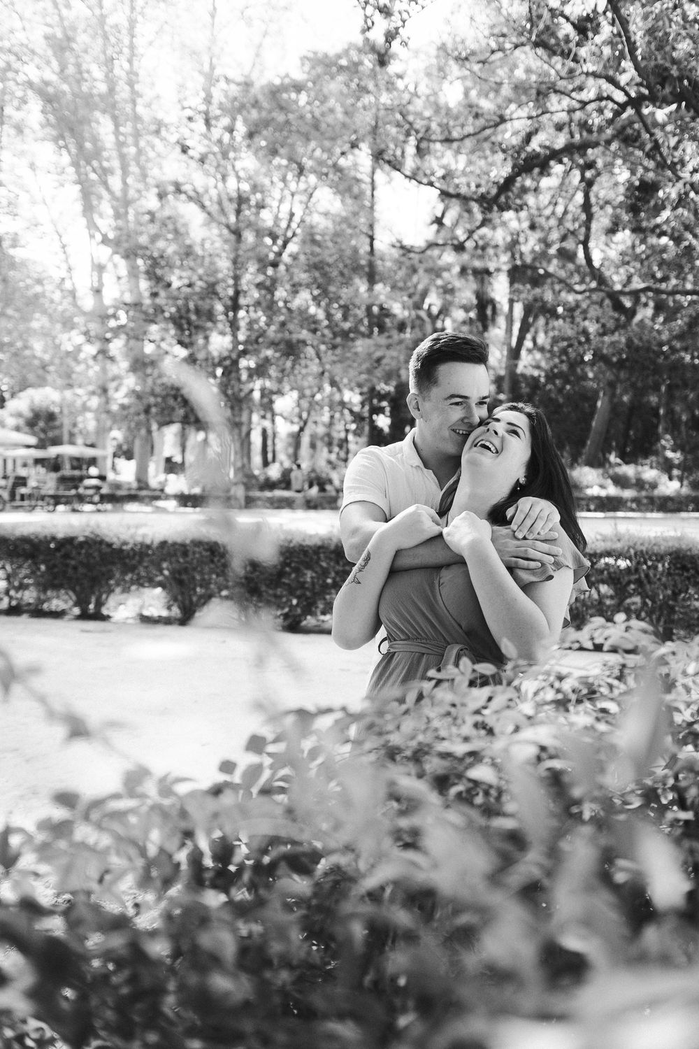 A romantic black and white photo of a couple embracing in a lush garden setting.