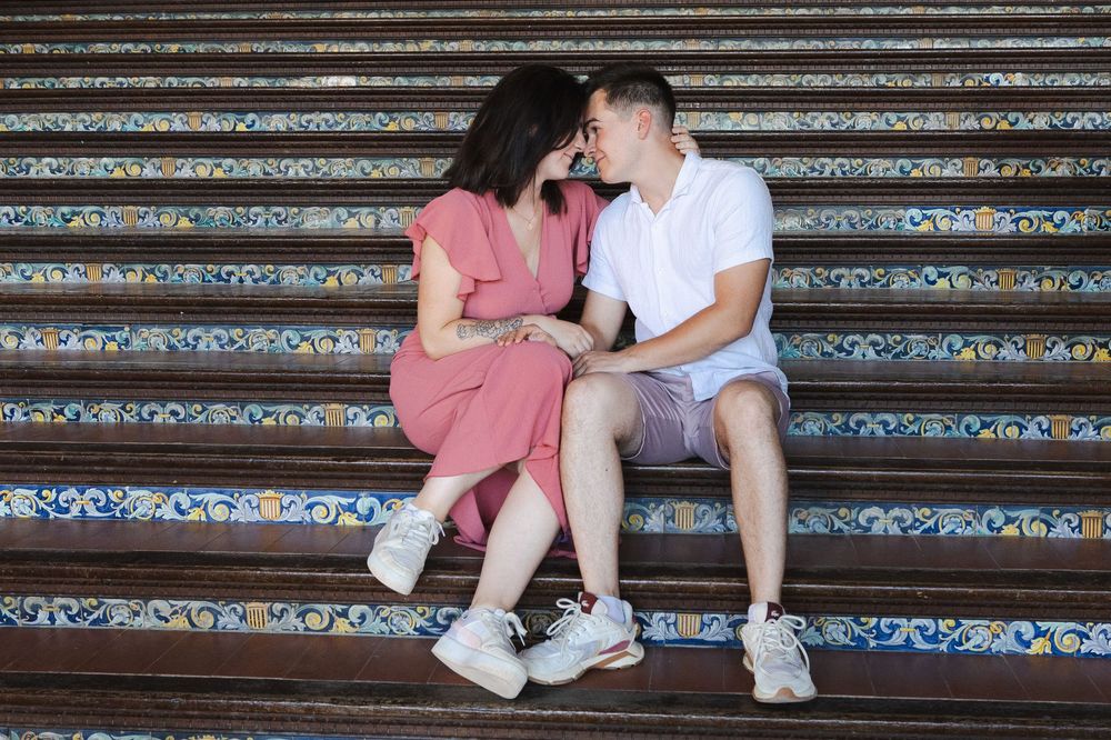 Two people sit together on colorful mosaic steps in casual summer attire.
